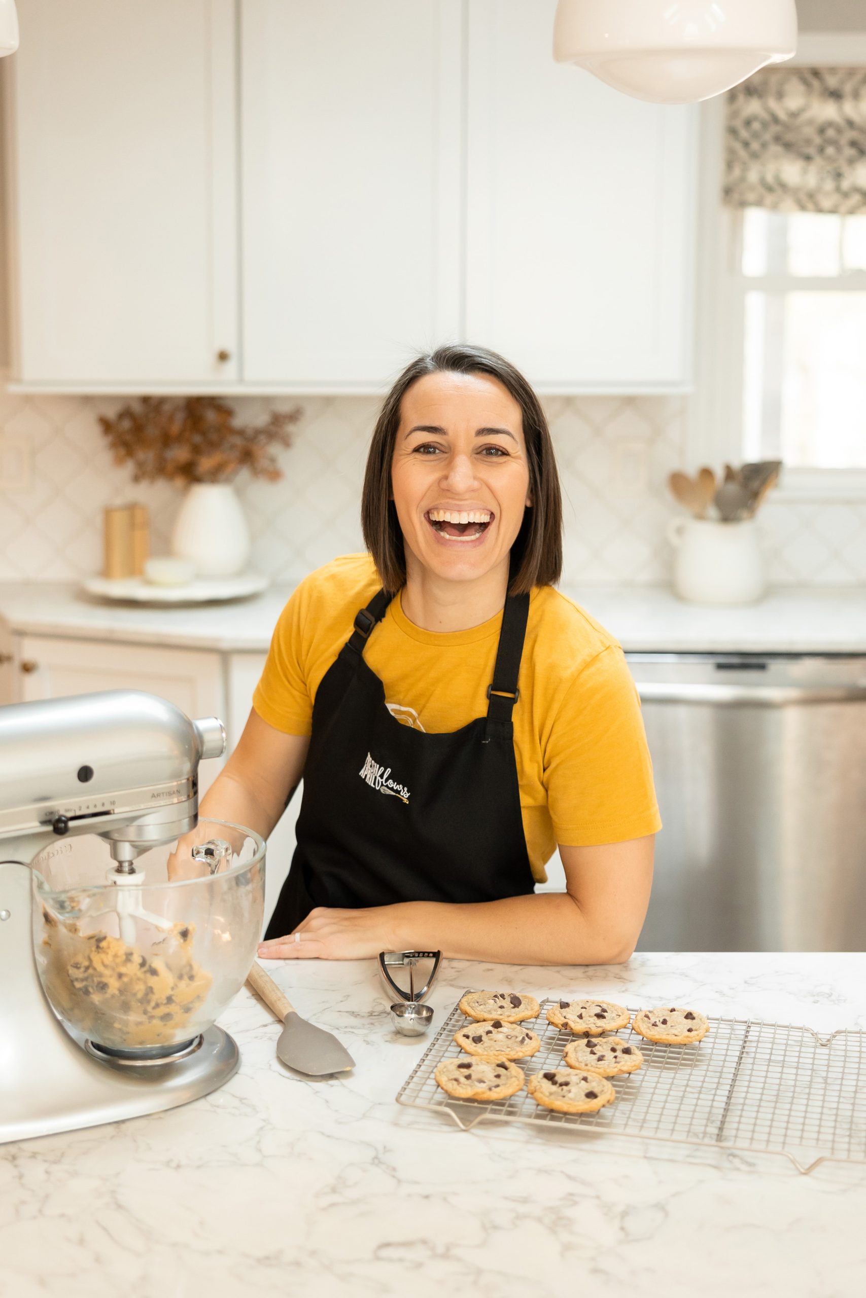 A woman in a kitchen with a mixer and cookies on the counter in front of her.